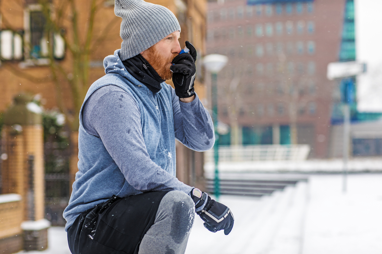 Man using asthma inhaler during an outdoor fitness session in cold, snowy weather