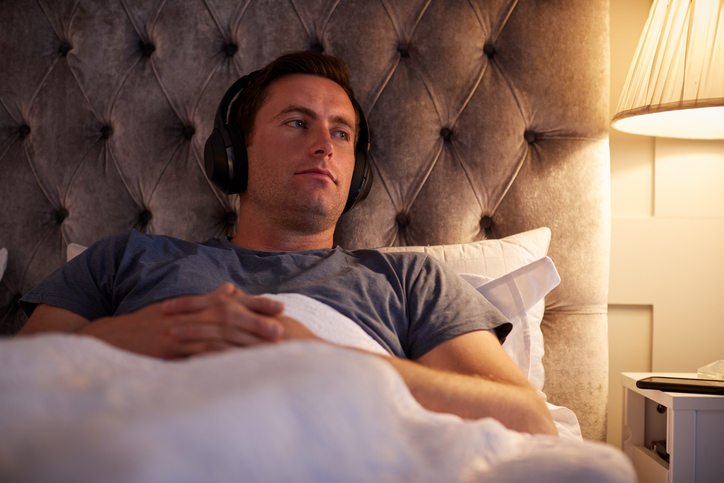 Man Wearing Wireless Headphones Listening To Music Before Going To Sleep