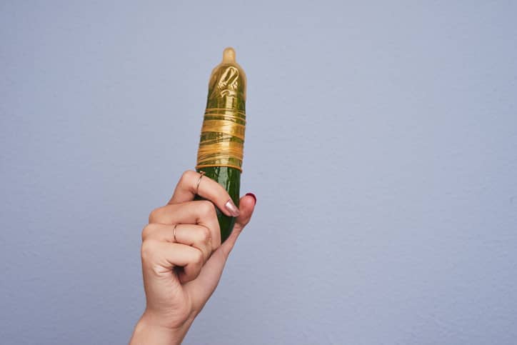 Person holding a cucumber in a condom