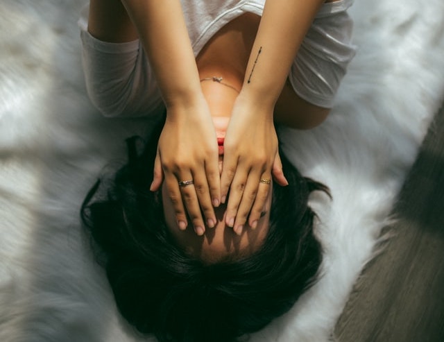 Person lying down and covering their face with their hands because they are stressed