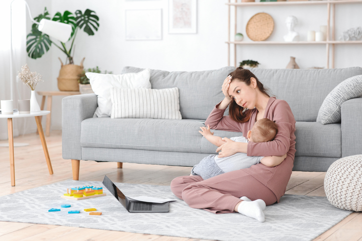  Tired young mom breastfeeding baby and working on laptop at home