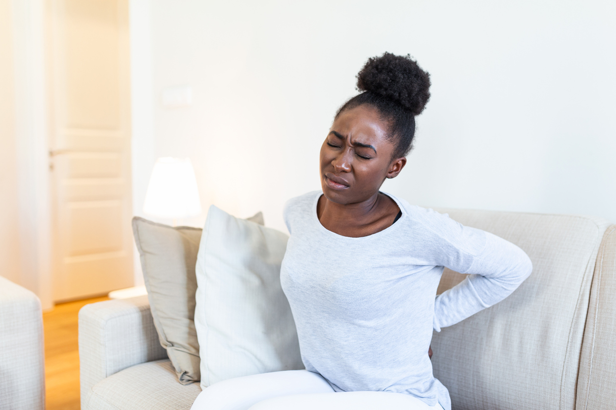 Woman sitting on a sofa with hands on her lower back, lower back pain